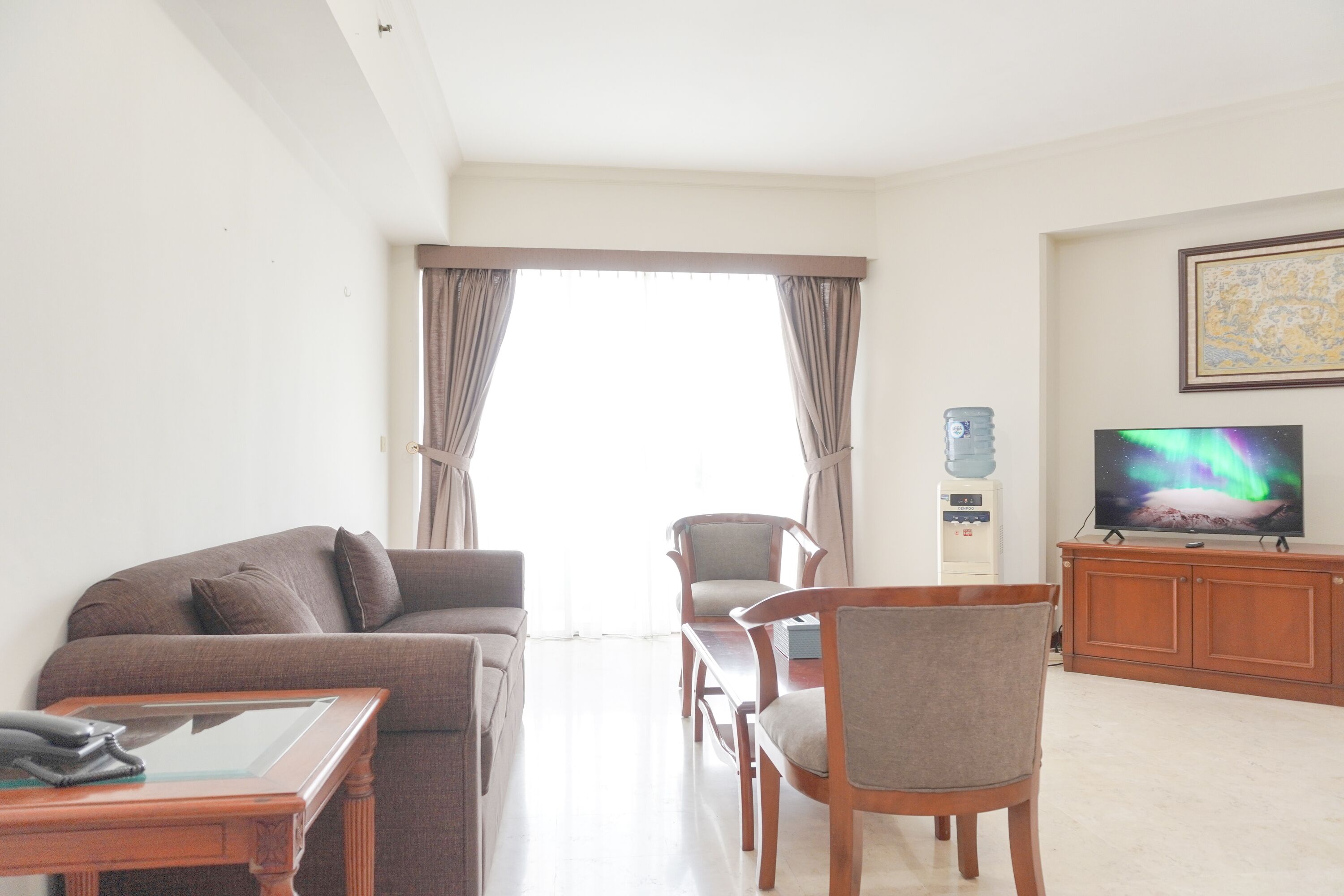 A living room with a sofa, chairs, a coffee table, a TV, and a water dispenser.