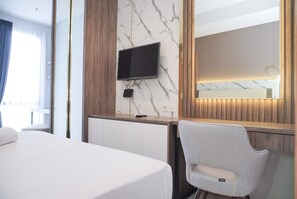 Une chambre d’hôtel avec un lit, un téléviseur fixé au mur en marbre, une chaise et un grand miroir.