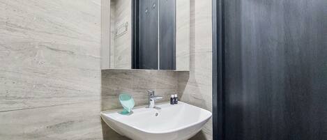Une salle de bain avec un lavabo blanc, un miroir et une porte sombre.