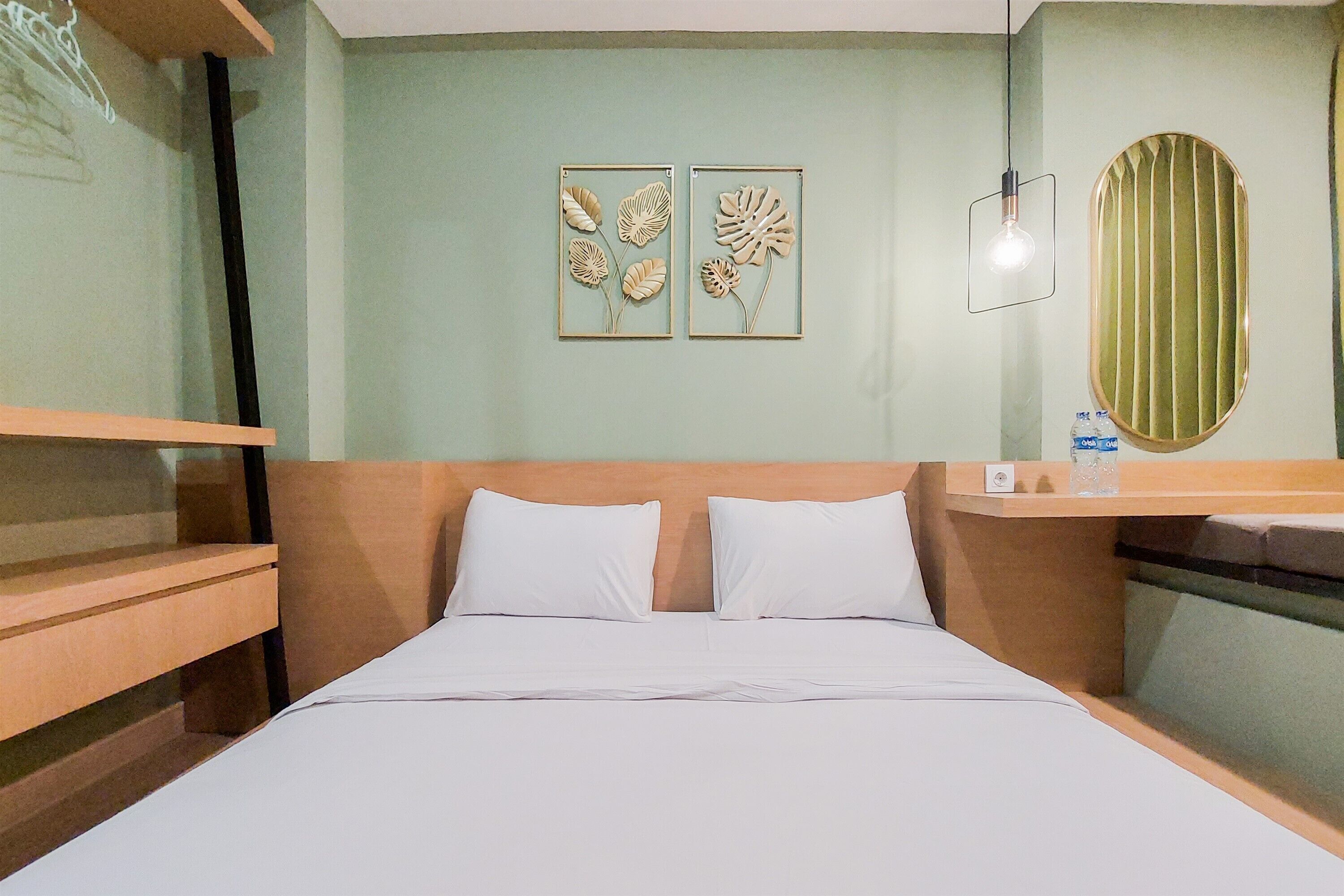 Hotellihuone, jossa on sänky, kaksi tyynyä, puinen pääty, seinään kiinnitetty valaisin ja kaksi kehystettyä, kukkateemalla koristeltua seinätaulua.