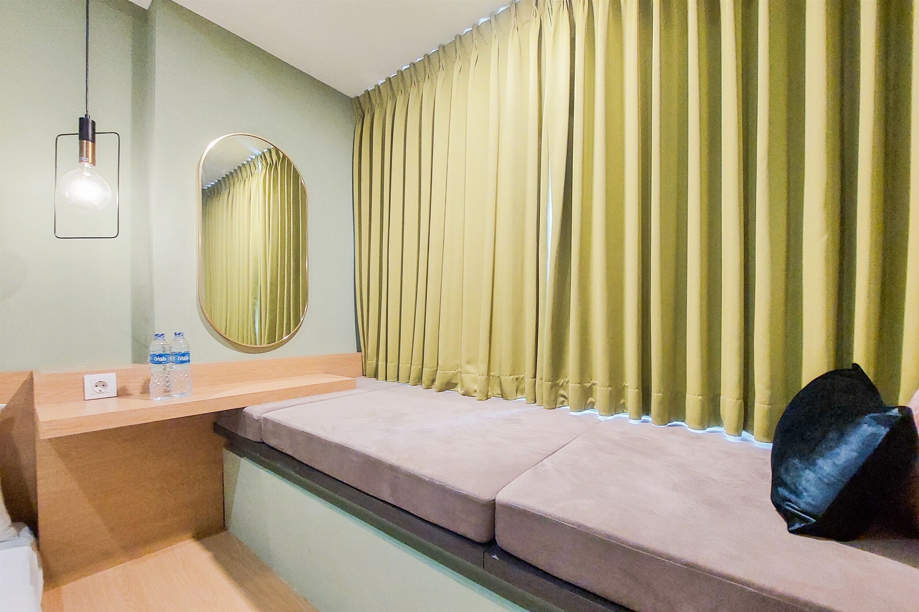A hotel room with a bed, a bedside table with a mirror, a water bottle, and a black bag.