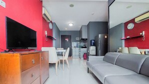 Ein modernes Wohnzimmer mit Flachbildfernseher, einem grauen Sofa, einem Holzkabinett und einem Essbereich mit Tisch und Stühlen.