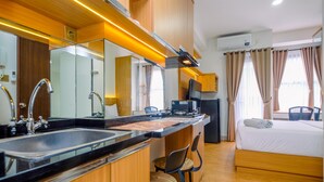 A modern hotel room with a kitchen area, a bed, and a seating area with chairs. - Comfort And Best Deal Studio Room Transpark Cibubur Apartment (Depok)