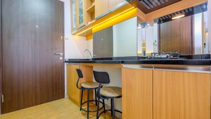 A modern kitchen with wooden cabinets, a black countertop, and two bar stools. - Comfort And Best Deal Studio Room Transpark Cibubur Apartment (Depok)