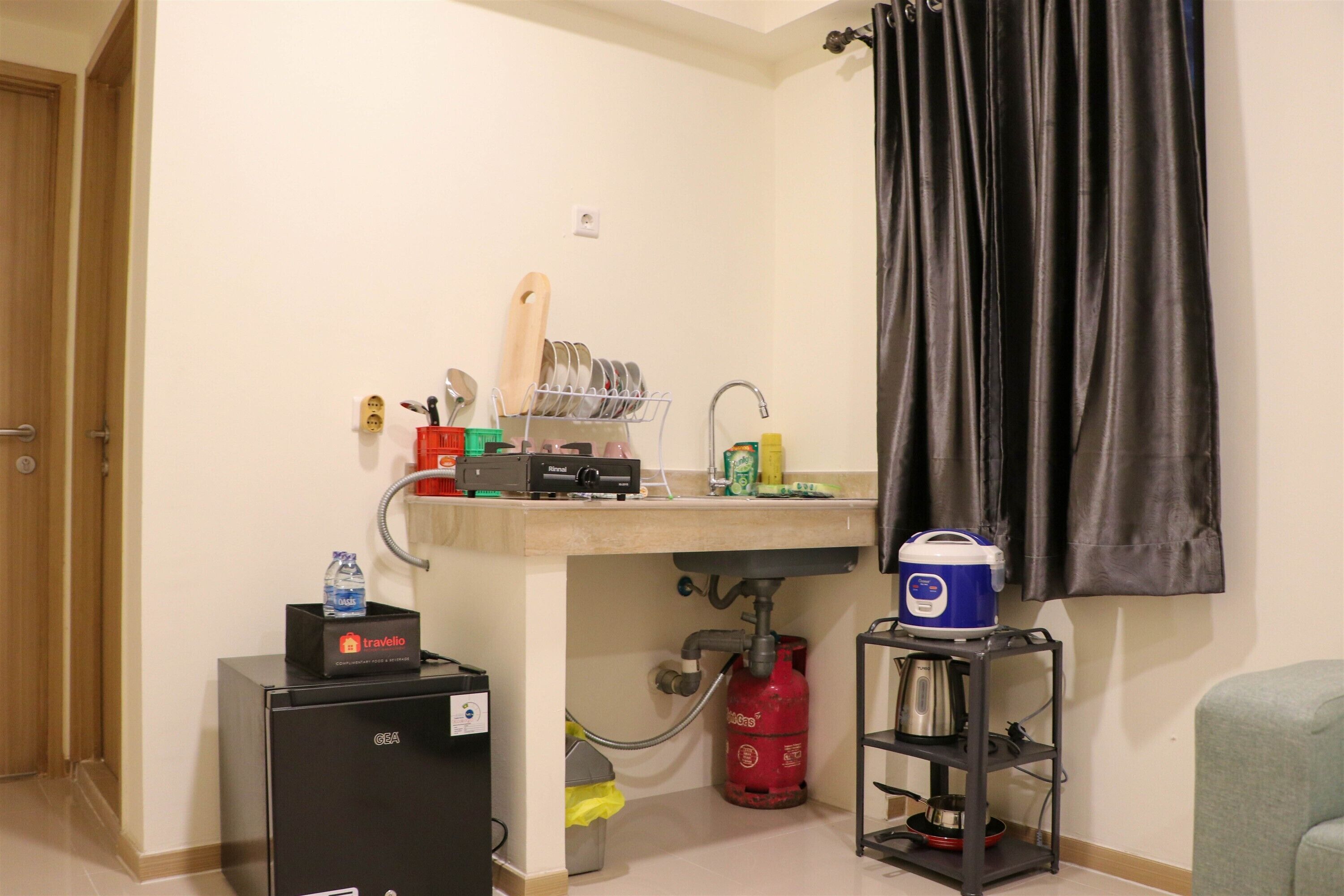 Una cocina compacta con un lavamanos, un refrigerador pequeño, una estufa a gas y un cilindro de gas portátil.