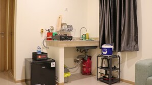 Una cocina compacta con un lavamanos, un refrigerador pequeño, una estufa a gas y un cilindro de gas portátil.