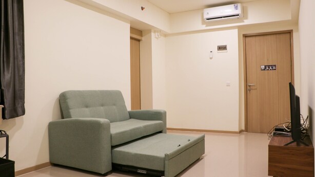 Una habitación con un sofá gris, una puerta de madera y un televisor sobre un mueble de madera.