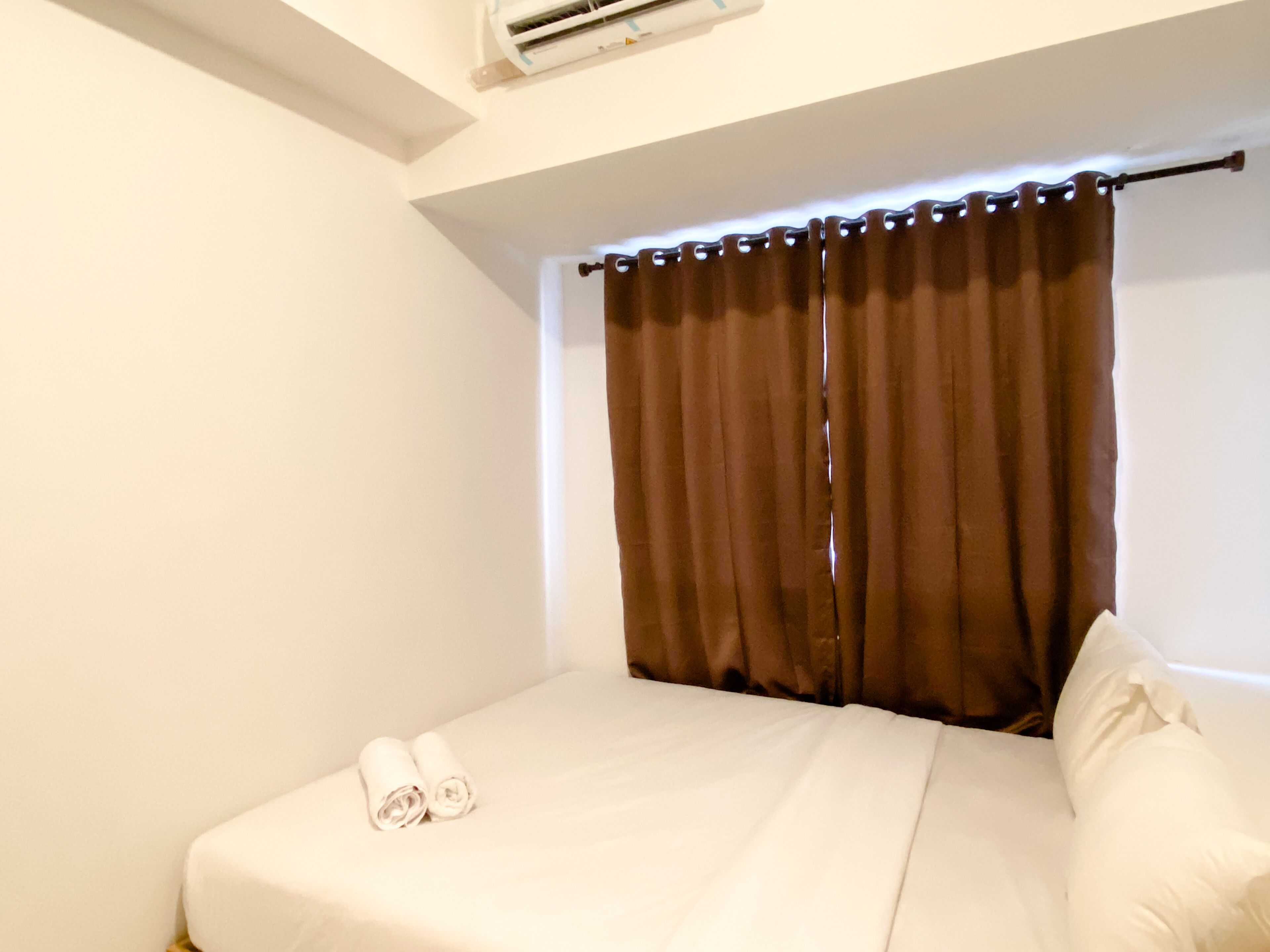 A small, clean room with a bed, a window with brown curtains, and a ceiling-mounted air conditioning unit.