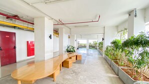 A modern indoor space with a long wooden bench, a red exit door, a fire hydrant, and potted plants along the walls. - Cozy 1Br Without Living Room Grand Kamala Lagoon Apartment (Bekasi)