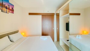 A hotel room with a large bed, a wooden wardrobe, a TV, and a painting on the wall. - Cozy 1Br Without Living Room Grand Kamala Lagoon Apartment (Bekasi)