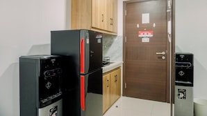 A compact kitchen with a refrigerator, a water dispenser, and wooden cabinets. - Nice And Modern Studio At 38Th Floor Pacific Garden Apartment (Tangerang)