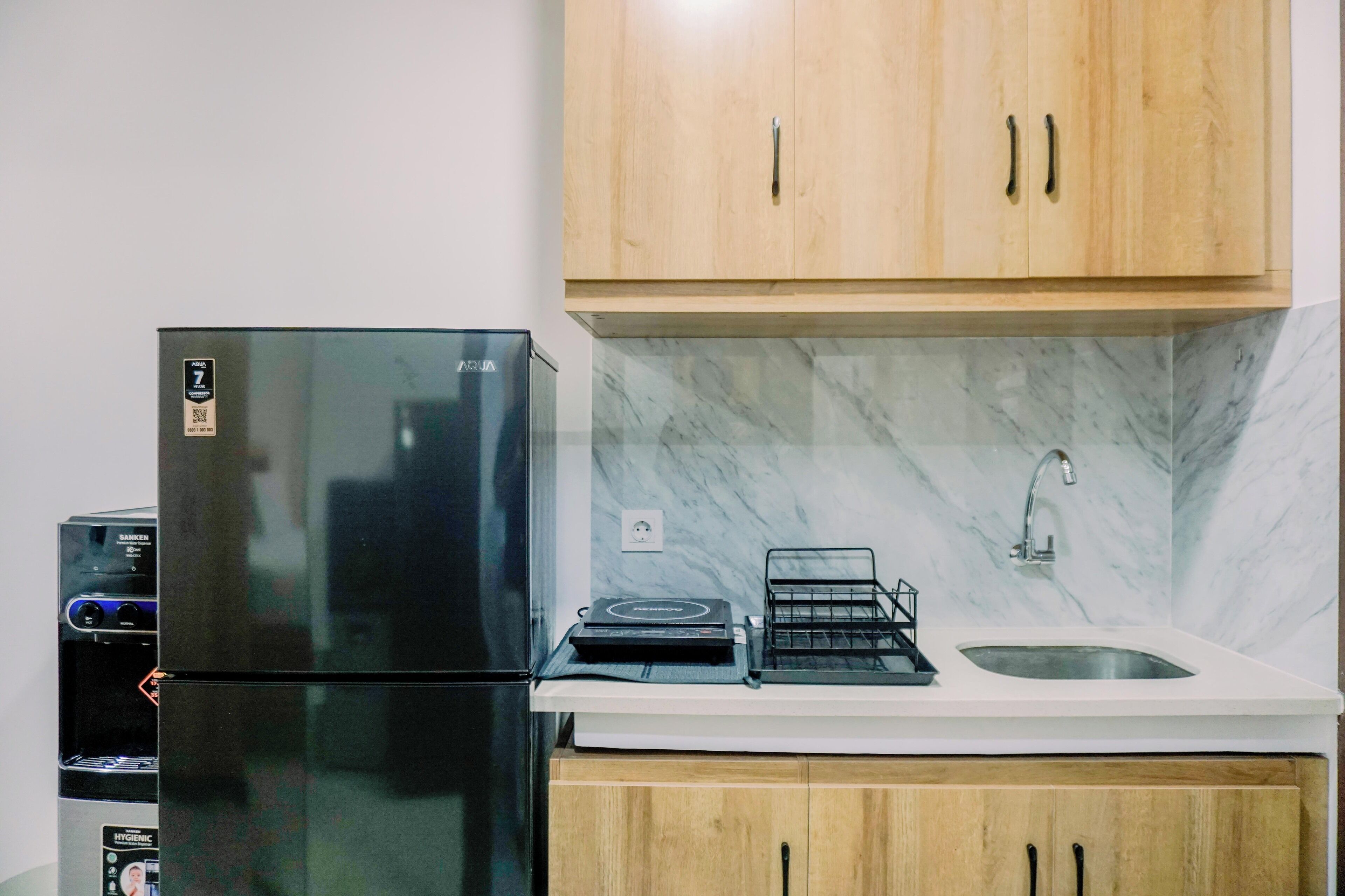 A kitchen with a black refrigerator, wooden cabinets, a marble backsplash, a sink, and a water dispenser.