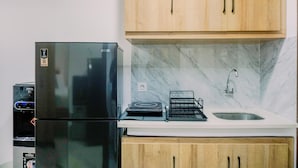 A kitchen with a black refrigerator, wooden cabinets, a marble backsplash, a sink, and a water dispenser. - Nice And Modern Studio At 38Th Floor Pacific Garden Apartment (Tangerang)