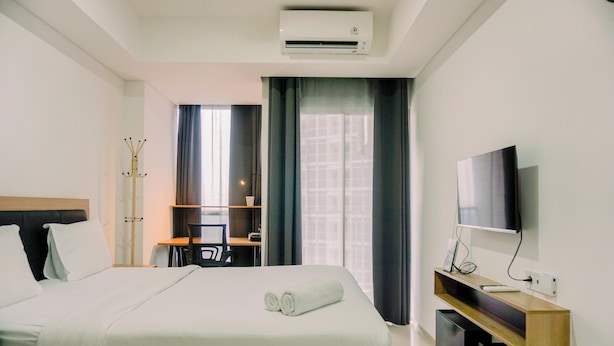 A hotel room with a bed, a desk, a TV, and an air conditioning unit. - Nice And Modern Studio At 38Th Floor Pacific Garden Apartment (Tangerang)