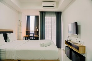 A hotel room with a bed, a desk, a TV, and an air conditioning unit. - Nice And Modern Studio At 38Th Floor Pacific Garden Apartment (Tangerang)