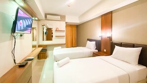 Une chambre d’hôtel avec deux lits, un téléviseur fixé au mur, un bureau avec un ordinateur et un miroir.