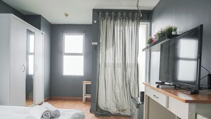 A hotel room with a bed, a desk, a television, and a window with curtains. - Nice And Warm Studio At Belmont Residence Puri Apartment (Jakarta)