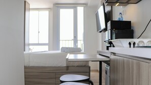 Ein modernes Zimmer mit einem Bett, einem kleinen Tisch, zwei Hocker, einem Fernseher und einer Küchenzeile.