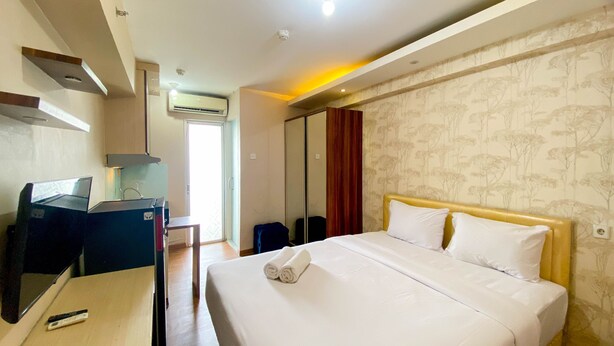 A hotel room with a bed, a desk, a chair, a wardrobe, and an air conditioning unit. - Good Deal And Comfy Studio At Bassura City Apartment (Jakarta)