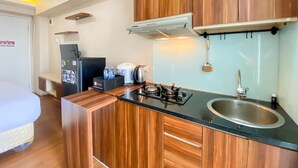 A compact kitchen with wooden cabinets, a black countertop, a stainless steel sink, and a built-in stove. - Good Deal And Comfy Studio At Bassura City Apartment (Jakarta)