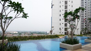 A rooftop swimming pool with a view of a cityscape, surrounded by greenery and modern buildings. - Good Deal And Comfy Studio At Bassura City Apartment (Jakarta)
