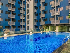 Une piscine dont le fond est recouvert de mosaïques bleues, entourée d’un bâtiment doté de balcons et d’une rambarde en verre.
