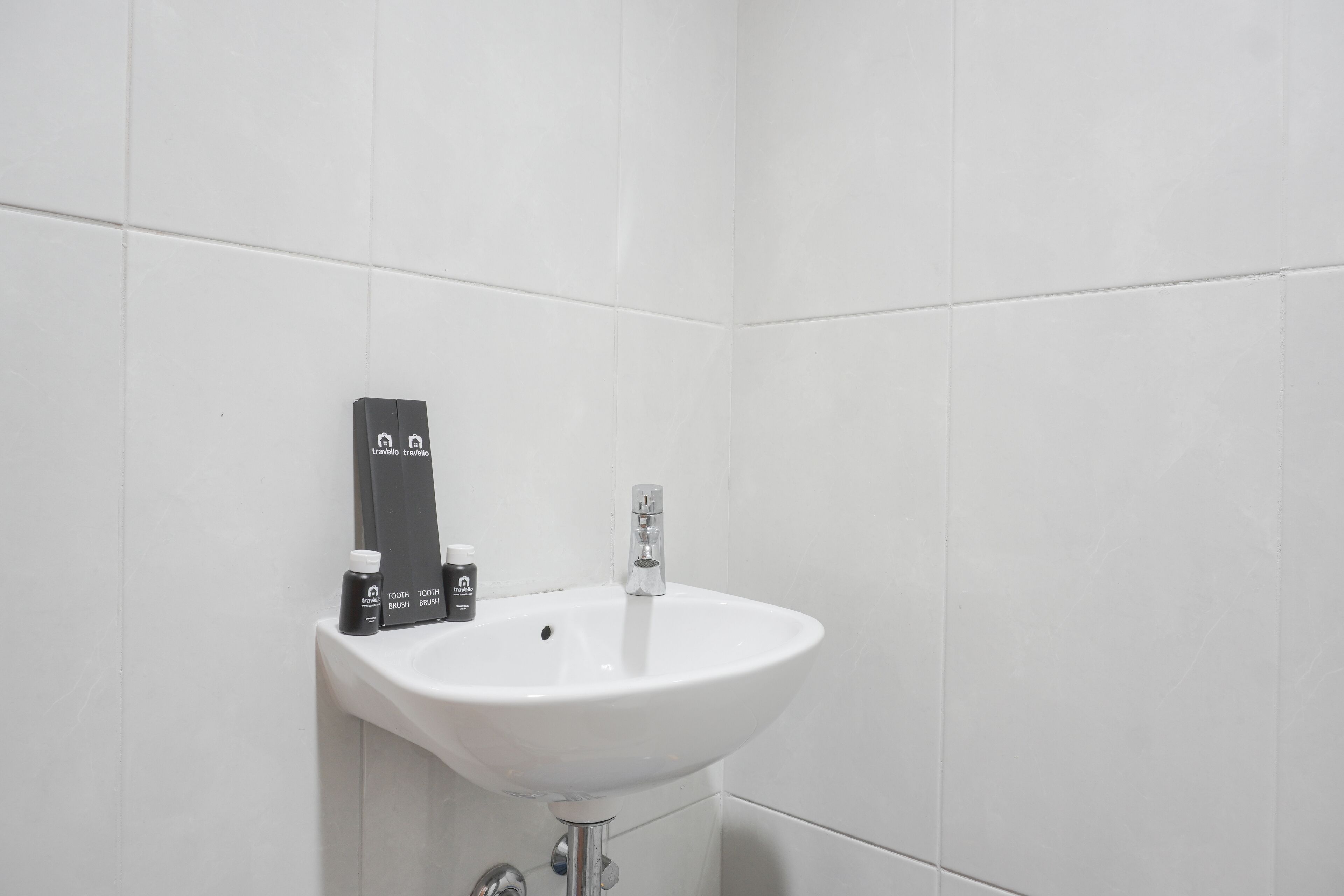 A white bathroom with a pedestal sink, a toothbrush holder, and a bottle of mouthwash.