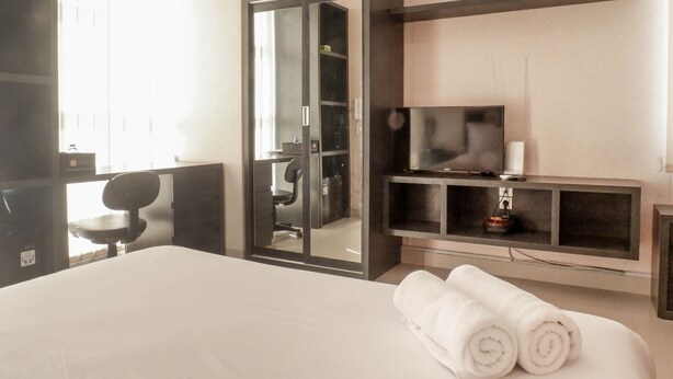 Ein Hotelzimmer mit einem großen Bett, einem Schreibtisch mit Stuhl, einem Fernseher auf einem Regal und einem Spiegel.