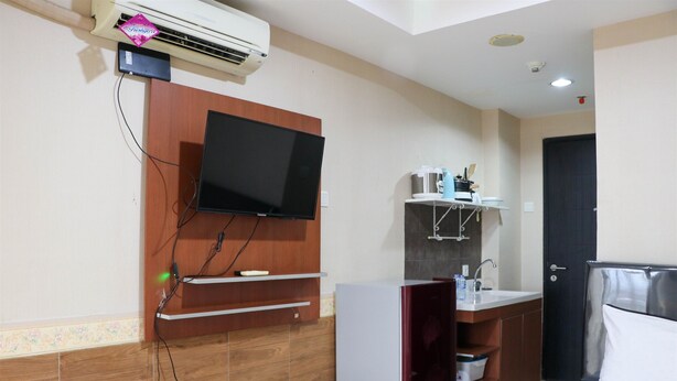 Une chambre d’hôtel avec un téléviseur fixé au mur, une petite kitchenette équipée d’un évier et un lit avec du linge de lit blanc.