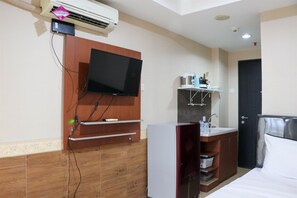A hotel room with a TV mounted on the wall, a small kitchenette with a sink, and a bed with white linens. - Comfort And Minimalist Studio At Belmont Residence Puri Apartment (Jakarta)