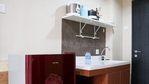 Une cuisine de taille réduite, dotée d’un plan de travail blanc, d’un évier et d’un meuble sous l’évier. Une bouteille d’eau est posée sur le plan de travail.