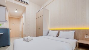 A hotel room with a large bed, a wooden wardrobe, a desk, and a wall-mounted light. - Simply Look And Comfort Studio Tree Park City Bsd Apartment (South Tangerang)