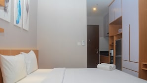 A hotel room with a bed, white bedding, a headboard, a wall-mounted light, and a door leading to a bathroom.