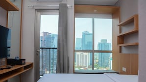 A hotel room with a bed, a TV, a desk, and a window with a city view.