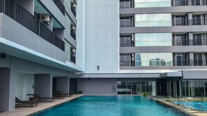 A modern building with a central swimming pool, balconies, and a covered seating area.