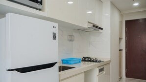 A modern kitchen with white cabinets, a white refrigerator, a blue container, and a gas stove. - Minimalist Studio At Sky House Bsd Apartment (Pagedangan)