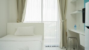 A bedroom with a bed, curtains, a TV, and a water bottle on a shelf. - Minimalist Studio At Sky House Bsd Apartment (Pagedangan)