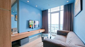 Ein modernes Hotelzimmer mit großem Fenster, einer Couch, einem Glastisch und einem flachbildfernseher an der Wand.