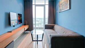 Ein modernes Hotelzimmer mit einer Couch, einem kleinen runden Tisch, einem Fernseher auf einer Holzkonsole und einem großen Fenster mit Vorhängen.