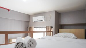 A hotel room with a bed, a wall-mounted air conditioner, a window with curtains, and a wooden headboard. - Comfy And Minimalist Studio Dave Apartment Near Universitas Indonesia (Depok)