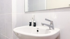 Un lavabo blanc dans la salle de bain, avec un robinet chromé, un miroir au-dessus et deux flacons de savon pour les mains placés sur le bord du lavabo.