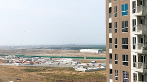 Un immeuble de grande hauteur doté de nombreux balcons, offrant une vue sur un chantier de construction avec des clôtures temporaires et des bâtiments en arrière-plan.