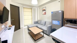 A modern kitchen with a built-in refrigerator and microwave, a grey sofa, a wooden coffee table, and a white countertop. - Exclusive And Comfortable 1Br Apartment Mustika Golf Residence (Cikarang)