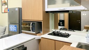 A compact kitchen with a refrigerator, microwave, stove, and wooden cabinets. - Exclusive And Comfortable 1Br Apartment Mustika Golf Residence (Cikarang)