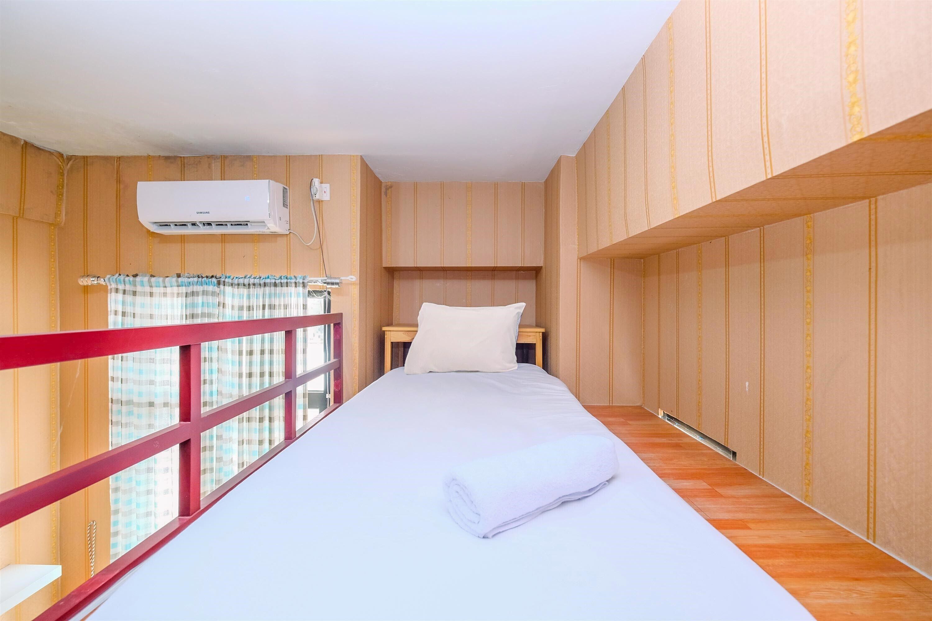 Una habitación con una cama, una ventana de marco rojo y un equipo de aire acondicionado.