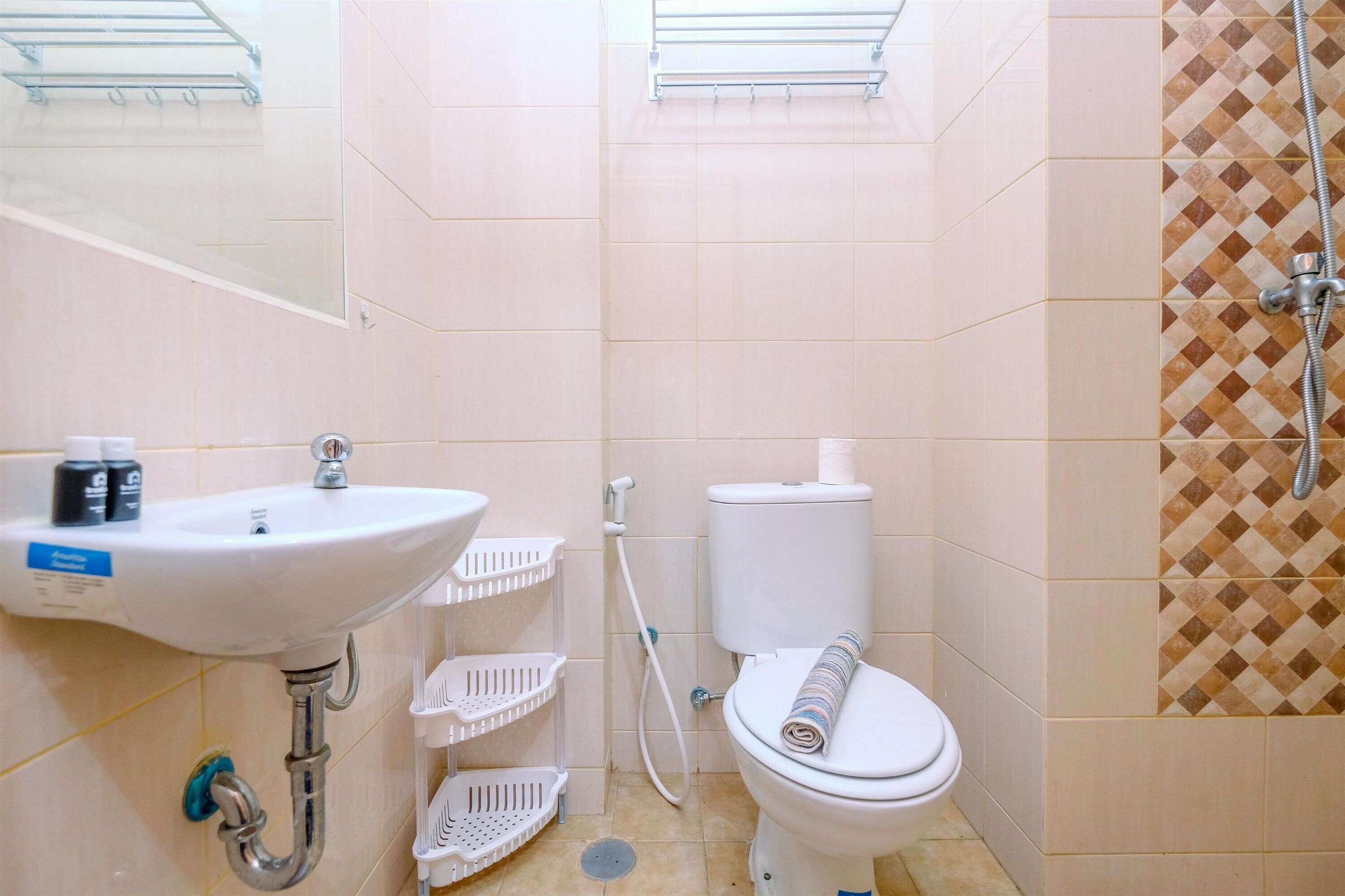 A bathroom with a white sink, toilet, and shower. There are white plastic baskets under the sink and a towel on the toilet.