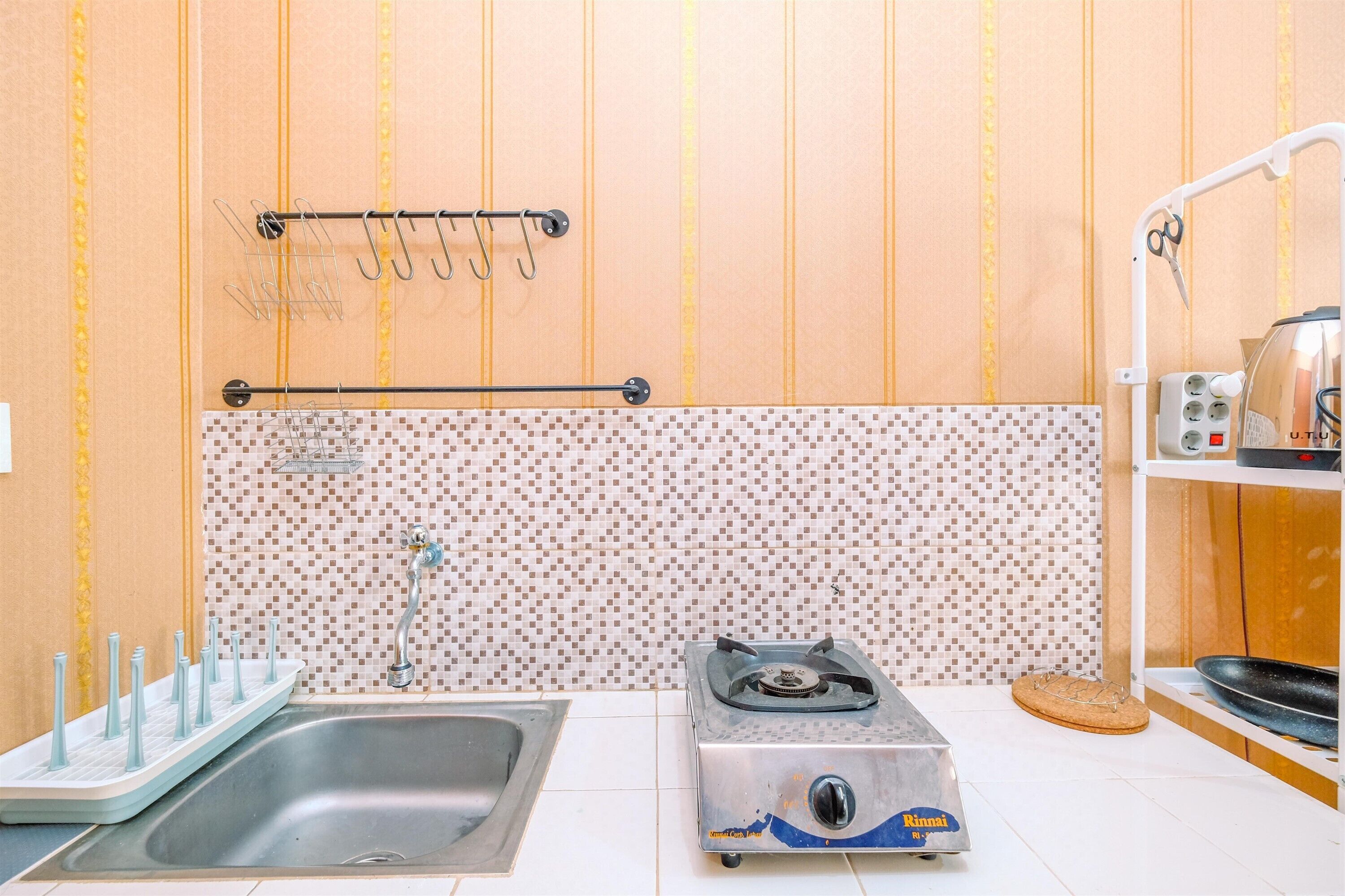 A kitchen with a sink, a gas stove, a tiled backsplash, and a utensil rack.