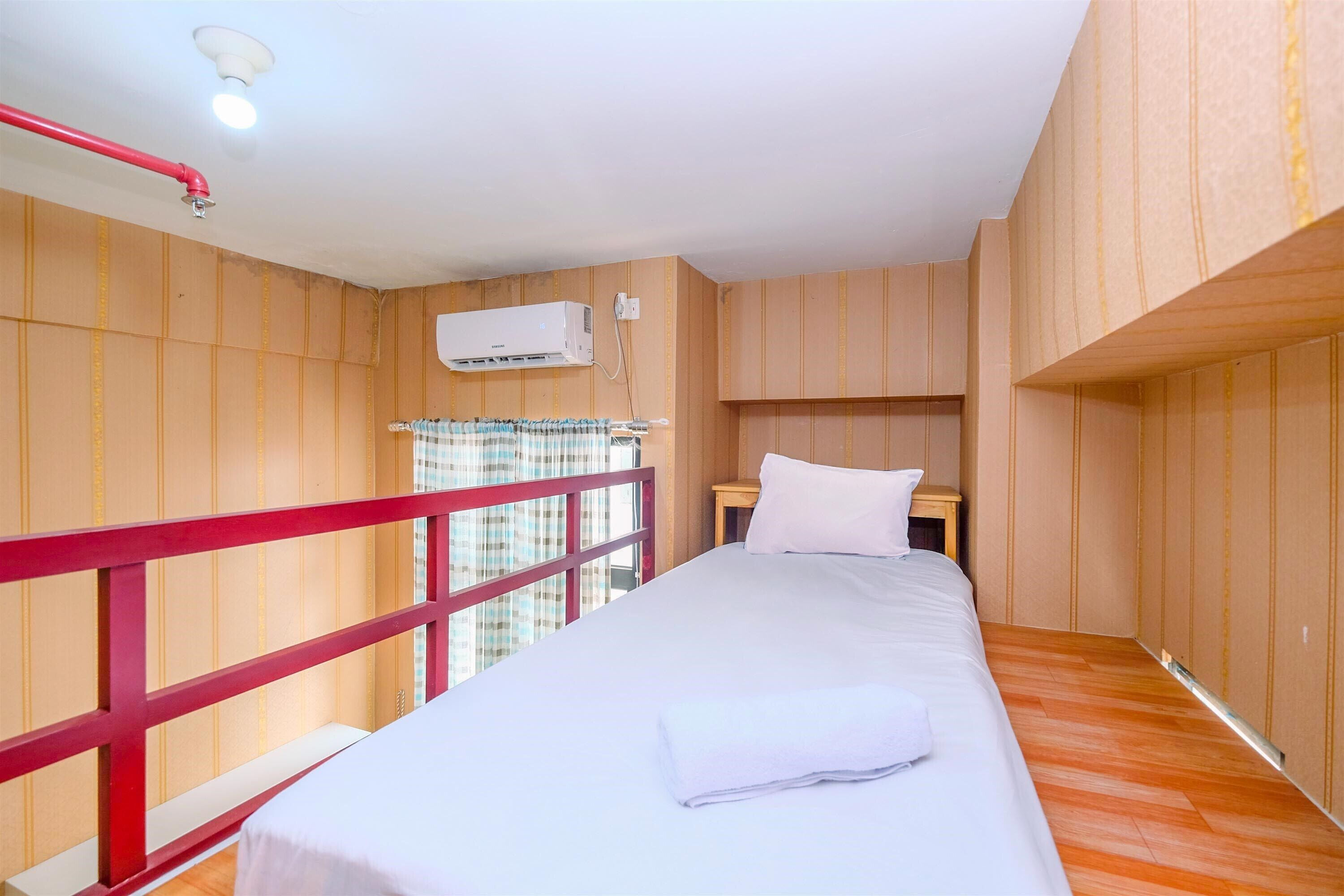 A hotel room with a wooden paneled wall, a red railing, a white bed, and an air conditioning unit.