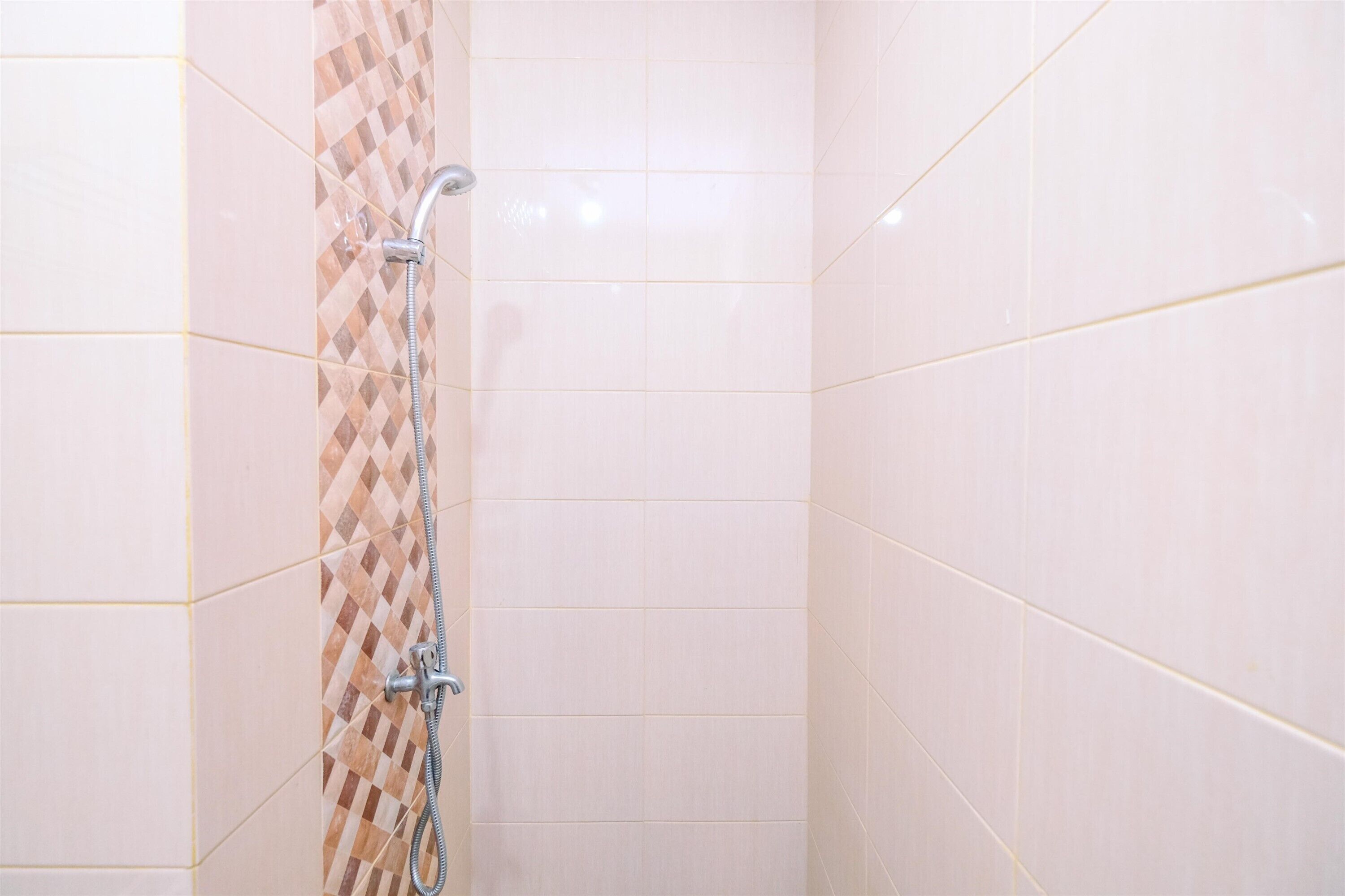 A shower with a checkered tile pattern on one wall and plain tiles on the other.