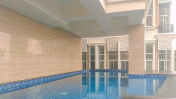 Una piscina interior con agua azul cristalina, paredes de azulejos y una terraza de madera.